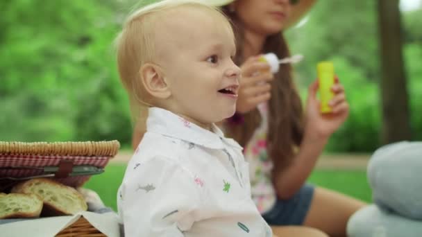 Petit enfant riant assis sur une couverture avec sa mère et sa sœur dans la forêt — Video