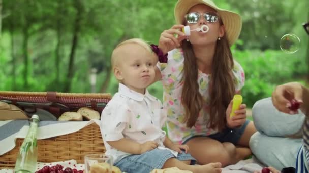Παιδί τρώει κεράσια στο πικνίκ. Μητέρα με παιδιά που χαλαρώνουν στο δάσος — Αρχείο Βίντεο