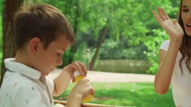 Park yerinde oğluyla eğlenen bir kadın. Neşeli çocuk dışarıda sabun köpüğü üflüyor.