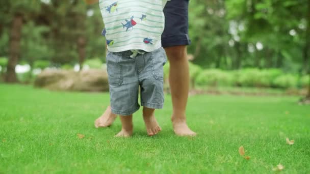 Niños piernas caminando sobre hierba verde en el parque. Hermano mayor enseñando a caminar a un niño — Vídeos de Stock