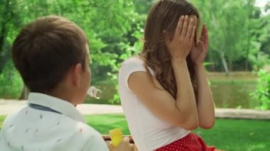 Anne parkta çocuklarla eğleniyor. Erkek ve kız sabun köpüğüyle oynuyorlar.