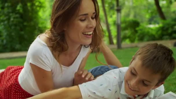 Madre abrazando al hijo. Mujer sonriente y niños acostados en una manta en el parque — Vídeos de Stock