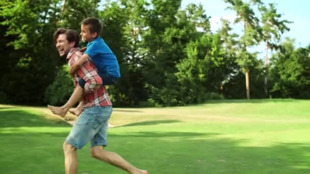 Un uomo che corre sul campo con un ragazzo sul retro. Padre dando figlio cavalcando — Video Stock