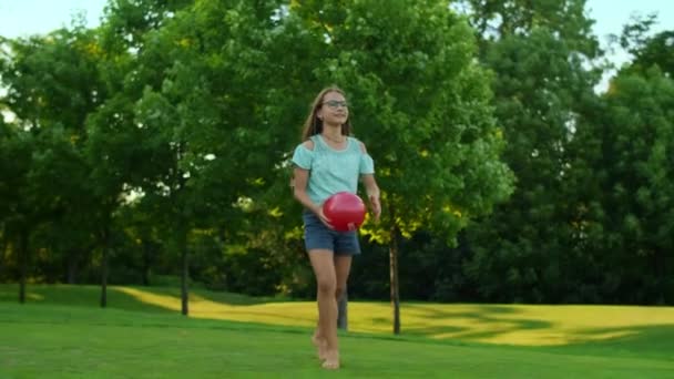Щаслива дівчина, що стоїть у зеленому полі. Красива дівчина тримає м'яч в руках — стокове відео