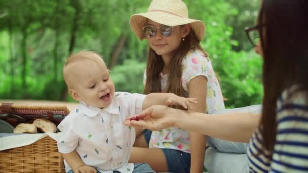 Moeder geeft kersen aan jongen bij de picknick. Gelukkige peuter die kersen eet — Stockvideo