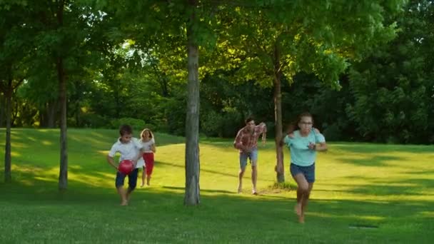 Niños con padres corriendo en el parque de verano. Familia alegre jugando en el prado — Vídeo de stock