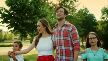 Çocuklar ve ebeveynler yaz parkında yürüyor. Baba kızını tutuyor.