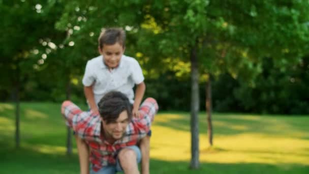 Jongen springt op de man terug in het veld. Portret van een gelukkige vader die zijn zoon terugdraagt — Stockvideo