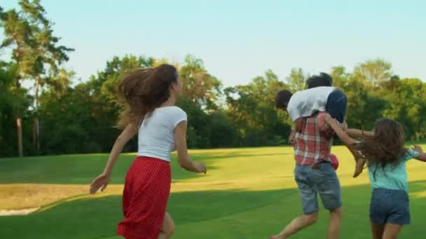 Rodzina biegnie w terenie. Szczęśliwe dzieci i rodzice bawią się piłką na łące — Wideo stockowe