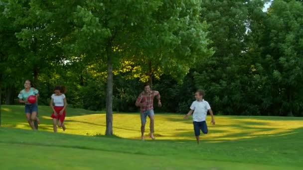 Familjen springer på grönt fält. Föräldrar och barn leker med bollen utomhus — Stockvideo