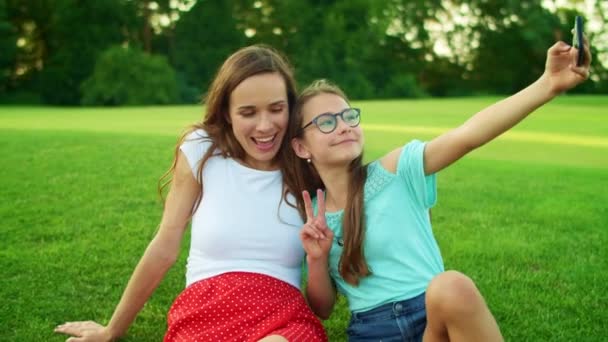 Frau und Mädchen sitzen auf Gras. Tochter macht Selfie mit Mutter auf Handy — Stockvideo