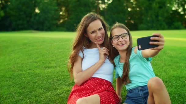 Ragazza e donna che parlano di selfie al cellulare. Figlia e madre seduta sull'erba — Video Stock
