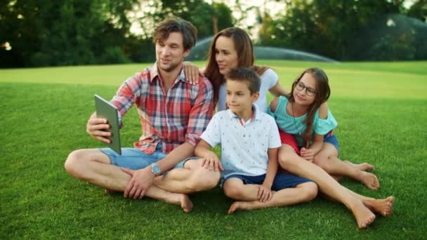 Homem segurando tablet digital com a família no parque. Pais e filhos usando almofada — Vídeo de Stock