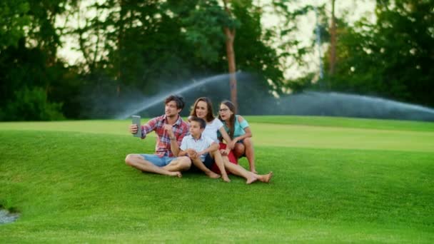 Familjen sitter på grön äng. Föräldrar och barn som använder digital surfplatta i parken — Stockvideo