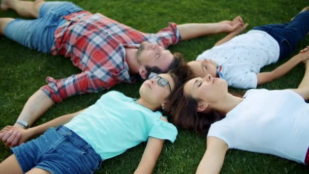 Οικογένεια ξαπλωμένη σε πράσινο γρασίδι σε κύκλο. Χαριτωμένα παιδιά και γονείς χαλαρώνουν στο πεδίο — Αρχείο Βίντεο