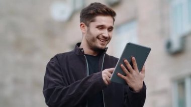 Dışarıda tablet ekranlı bir adam var. Mutlu adam mesaj tableti okuyor.
