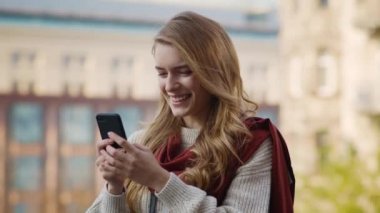 Dışarıdaki telefon ekranına bakan heyecanlı kız. Caddede telefonu tutan neşeli kadın.