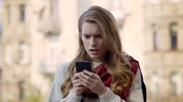 Zszokowana kobieta trzymająca telefon na zewnątrz. Rozczarowana dziewczyna patrząc ekran telefonu — Wideo stockowe