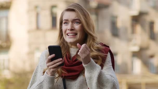 Vrolijke vrouw die met de telefoon springt. Opgewonden meisje op zoek mobiele telefoon op straat. — Stockvideo