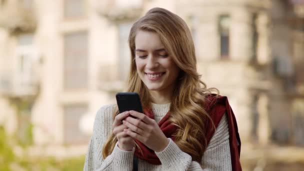 Glückliches Mädchen, das draußen mit dem Smartphone SMS schreibt. Fröhliche Frau telefoniert auf der Straße.