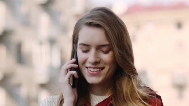 Улыбающаяся девушка говорит по телефону на улице. Счастливая женщина с телефоном на улице — стоковое видео