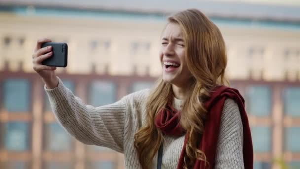 Lycklig flicka som drar ansikten med telefon utomhus. Skrattande kvinna med mobiltelefon. — Stockvideo