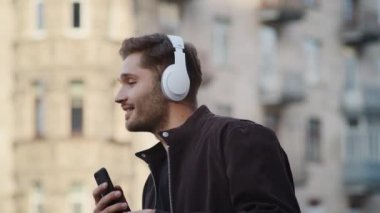 Hippi adam dışarıda kulaklıkla dans ediyor. Telefonda müzik dinleyen mutlu adam..