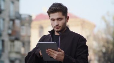 Genç adam dışarıda tablet kullanıyor. Hippi görünümlü cihaz ekranı açık havada.