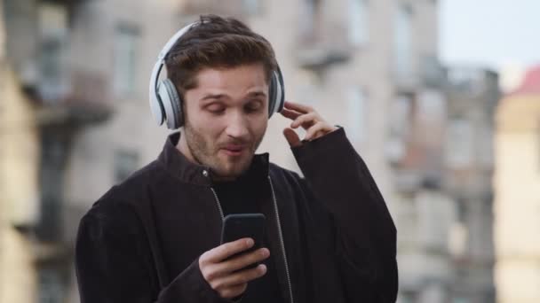 Un gars heureux écoutant des écouteurs de musique dehors. Homme souriant dansant dans la rue de la ville — Video