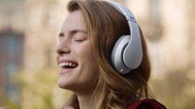 Dışarıda kulaklıkla gevşeyen neşeli bir kadın. Güzel kız yüzü müzik dinliyor.