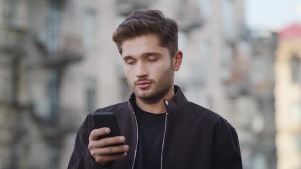 Il tizio hipster riceve messaggi al telefono fuori. Uomo sorridente che cerca schermo del telefono — Video Stock