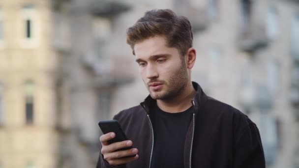 Un homme énervé qui utilise son téléphone dehors. gars ennuyé regarder écran sur la rue. — Video