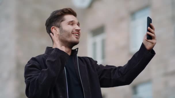笑顔の男は屋外で電話画面を見て。路上でビデオ通話をしている幸せな男 — ストック動画