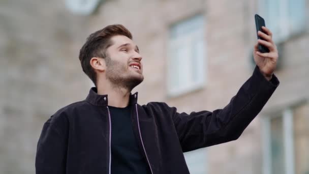 Un tipo feliz haciendo videollamadas afuera. Emocionado hombre mirando la pantalla del teléfono al aire libre — Vídeo de stock