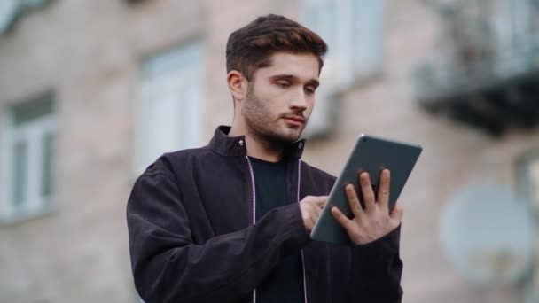 Lächelnder Typ, der draußen Nachrichten liest. Glücklicher Mann mit Tablet auf der Straße — Stockvideo