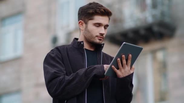 Tipo guapo mirando pantalla de la tableta al aire libre. Hombre joven tocando tableta digital . — Vídeo de stock