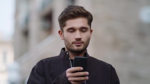 Překvapený muž používá venku telefon. Usmívající se chlap čtení zprávy na telefonu venku — Stock video