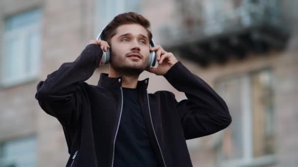 Un tipo feliz escuchando música con auriculares al aire libre. Hombre encantador bailando afuera — Vídeos de Stock