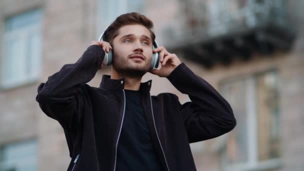 Un ragazzo felice che ascolta musica con le cuffie all'aperto. Uomo ricco che balla fuori — Video Stock