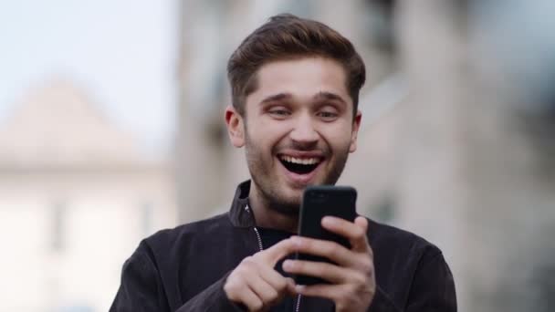 Homem feliz usando o telefone lá fora. Cara surpreso usando telefone celular ao ar livre . — Vídeo de Stock