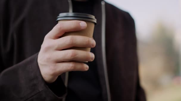 Mão de homem trazendo café takeaway a lábios. Guy mão segurando copo de papel ao ar livre . — Vídeo de Stock