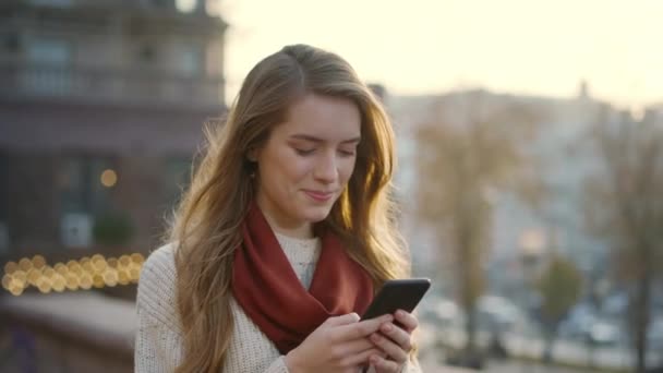 Menina feliz mensagens de texto telefone celular ao ar livre. Mulher alegre segurando telefone nas mãos — Vídeo de Stock