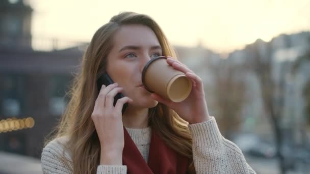 若い女性は携帯電話で歩く。女の子は手にコーヒーと電話を話す — ストック動画