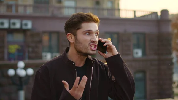 Angry man shouting on mobile phone outdoors. Anxious guy speaking cellphone.