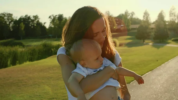 Mulher segurando menino em mãos no parque. Bela mãe abraçando filho no prado — Fotografia de Stock