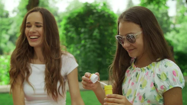 Mulher e menina brincando com bolhas de sabão no parque. Família rindo ao ar livre — Fotografia de Stock