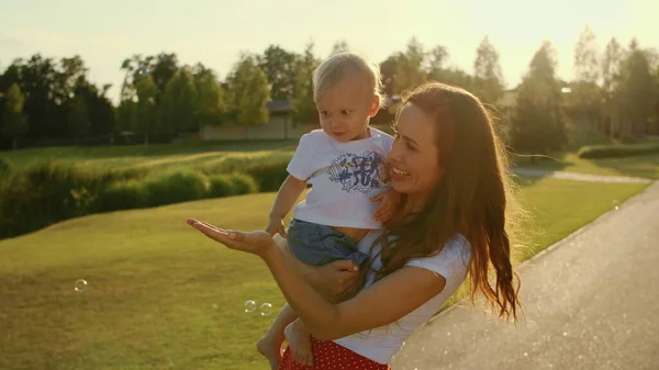 Femme tenant le garçon sur les mains. Enfant avec mère jouant avec des bulles de savon — Photo