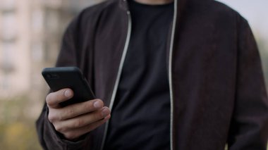 Erkek eli telefon ekranına dokunuyor. Dışarıda cep telefonuyla konuşan çekici bir adam..