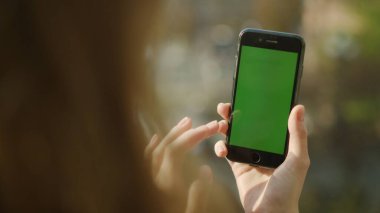 Yeşil ekranlı telefon kullanan kadın eller. Kız elleri açık havada telefon tutuyor..