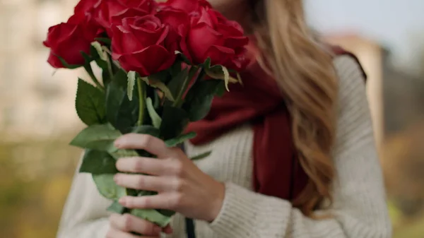 Женские руки, приносящие розы в лицо. Веселая девушка нюхает цветы на открытом воздухе — стоковое фото